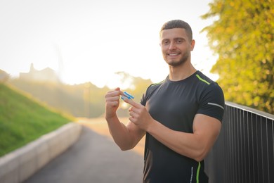 Attractive happy man checking pulse with blood pressure monitor on finger after training in park. Space for text