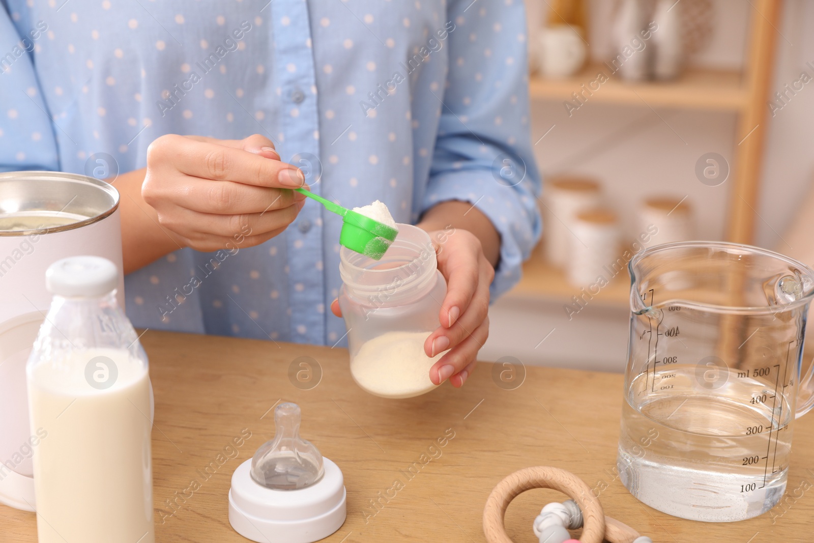 Photo of Woman preparing infant formula at table indoors, closeup. Baby milk