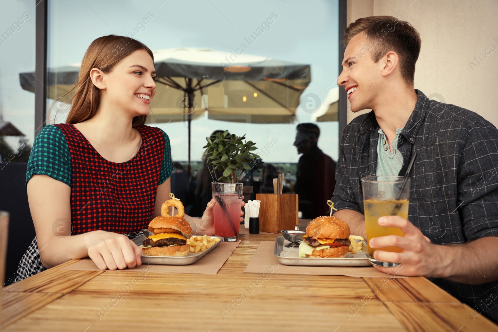 Photo of Young happy couple with burgers in street cafe