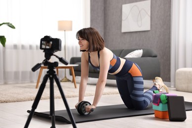 Photo of Happy sports blogger training with ab roller while recording fitness lesson at home