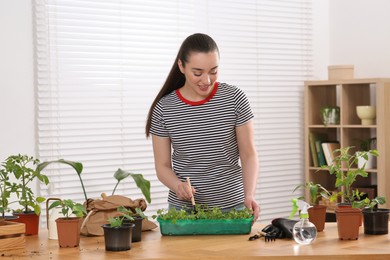 Photo of Happy woman planting seedlings into plastic container at wooden table in room