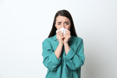 Young woman with tissue suffering from runny nose on white background