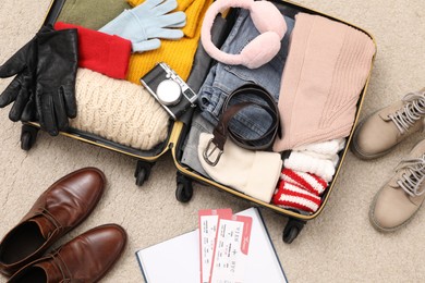 Photo of Open suitcase with warm clothes, accessories and shoes on floor, flat lay