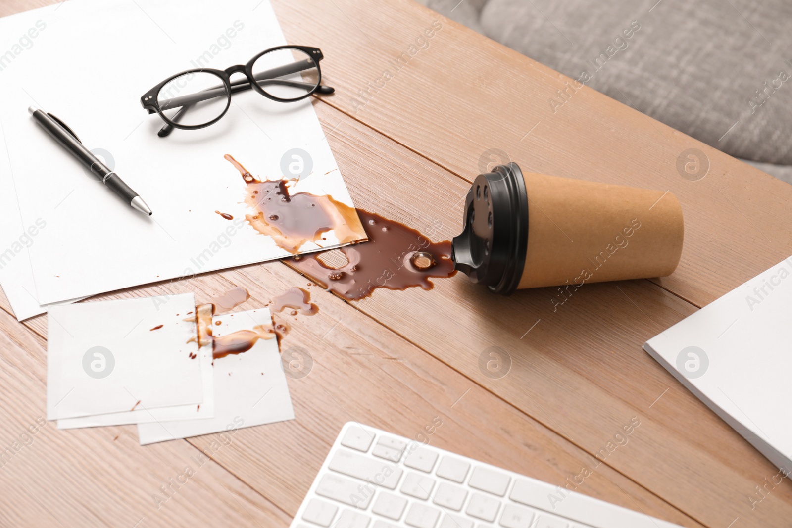 Photo of Paper cup with coffee spill on wooden office desk