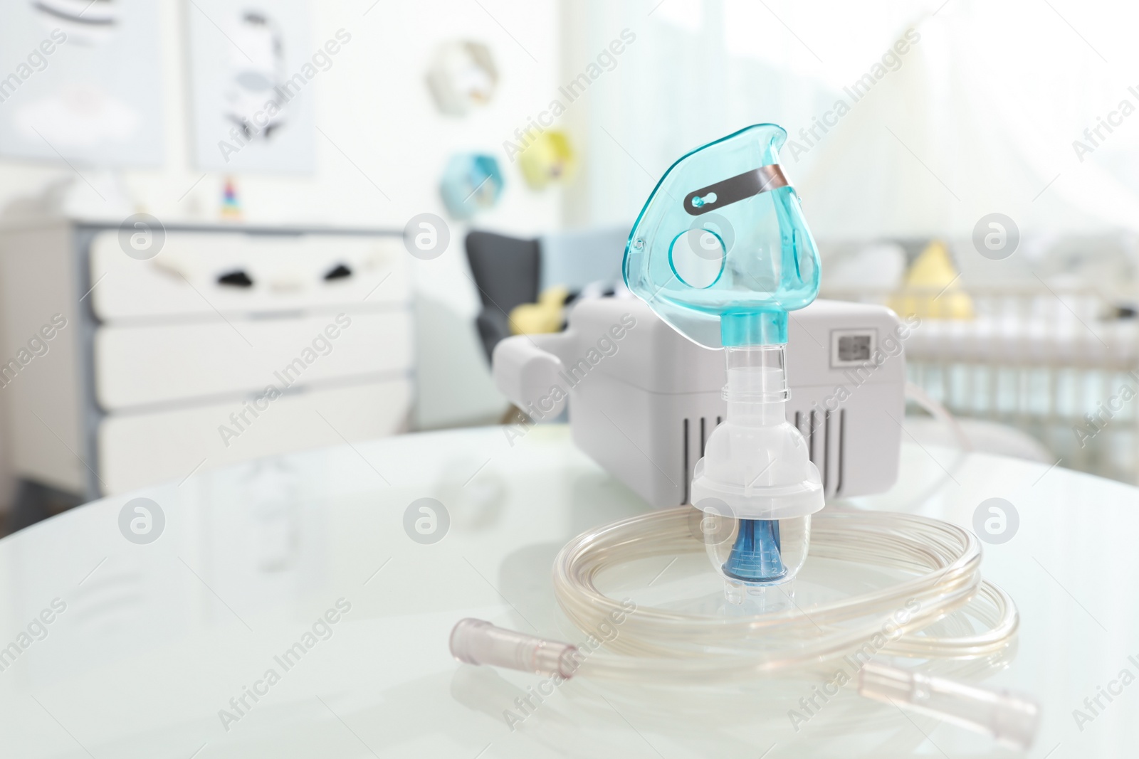 Photo of Modern nebulizer with face mask on white table in children's room. Equipment for inhalation