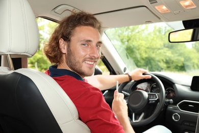 Attractive young man driving his luxury car, view from backseat