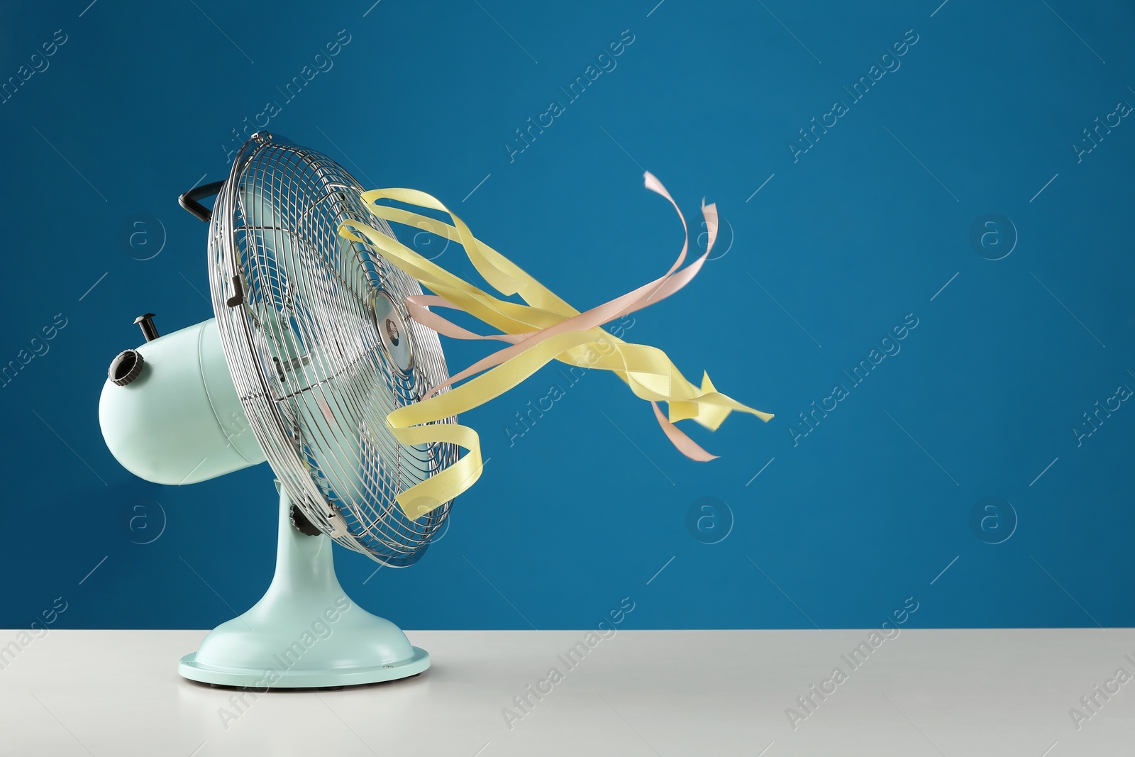 Photo of Electric fan on white table against blue background. Summer heat