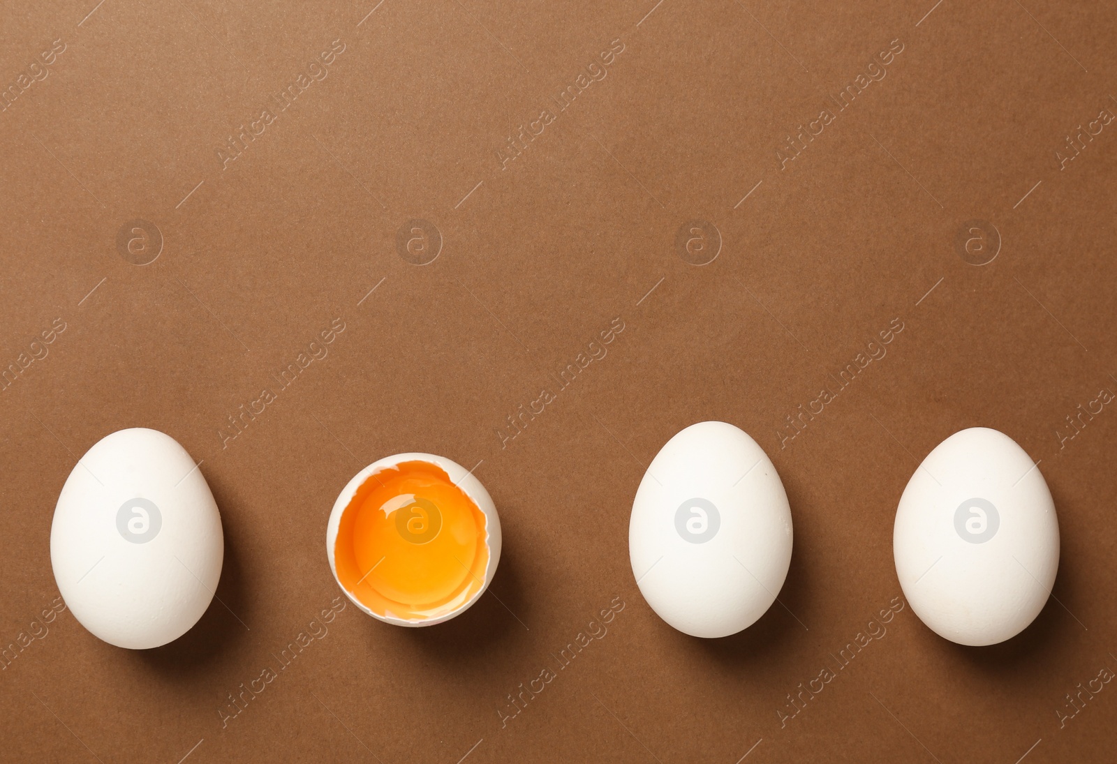 Photo of Whole and broken chicken eggs on brown background, flat lay. Space for text