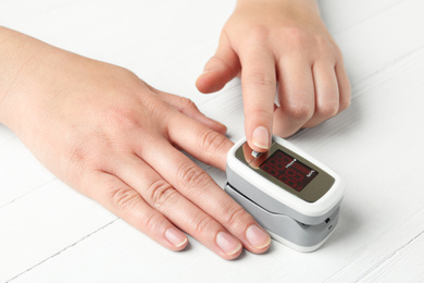 Photo of Woman using fingertip pulse oximeter at white wooden table, closeup