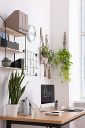 Photo of Cozy workplace with computer, modern furniture and houseplants at home