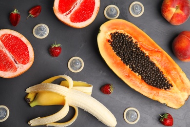 Photo of Flat lay composition with condoms and exotic fruits on black stone background. Erotic concept