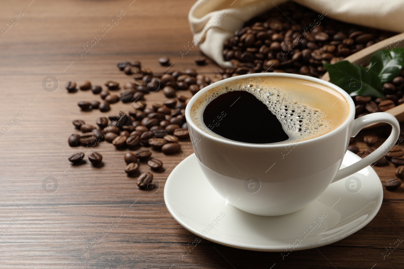 Photo of Cup of aromatic hot coffee and beans on wooden table, space for text