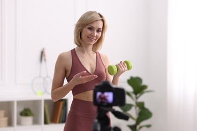 Smiling sports blogger with dumbbell recording fitness lesson with camera at home