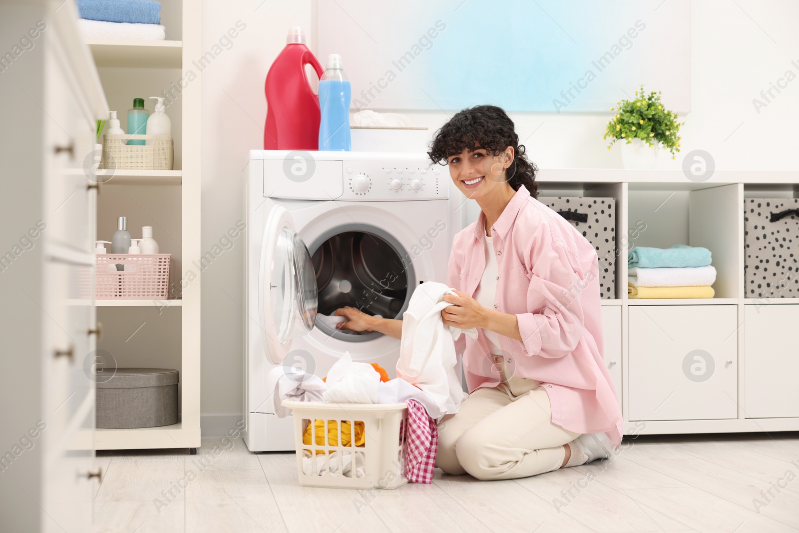 Photo of Happy woman putting laundry into washing machine indoors