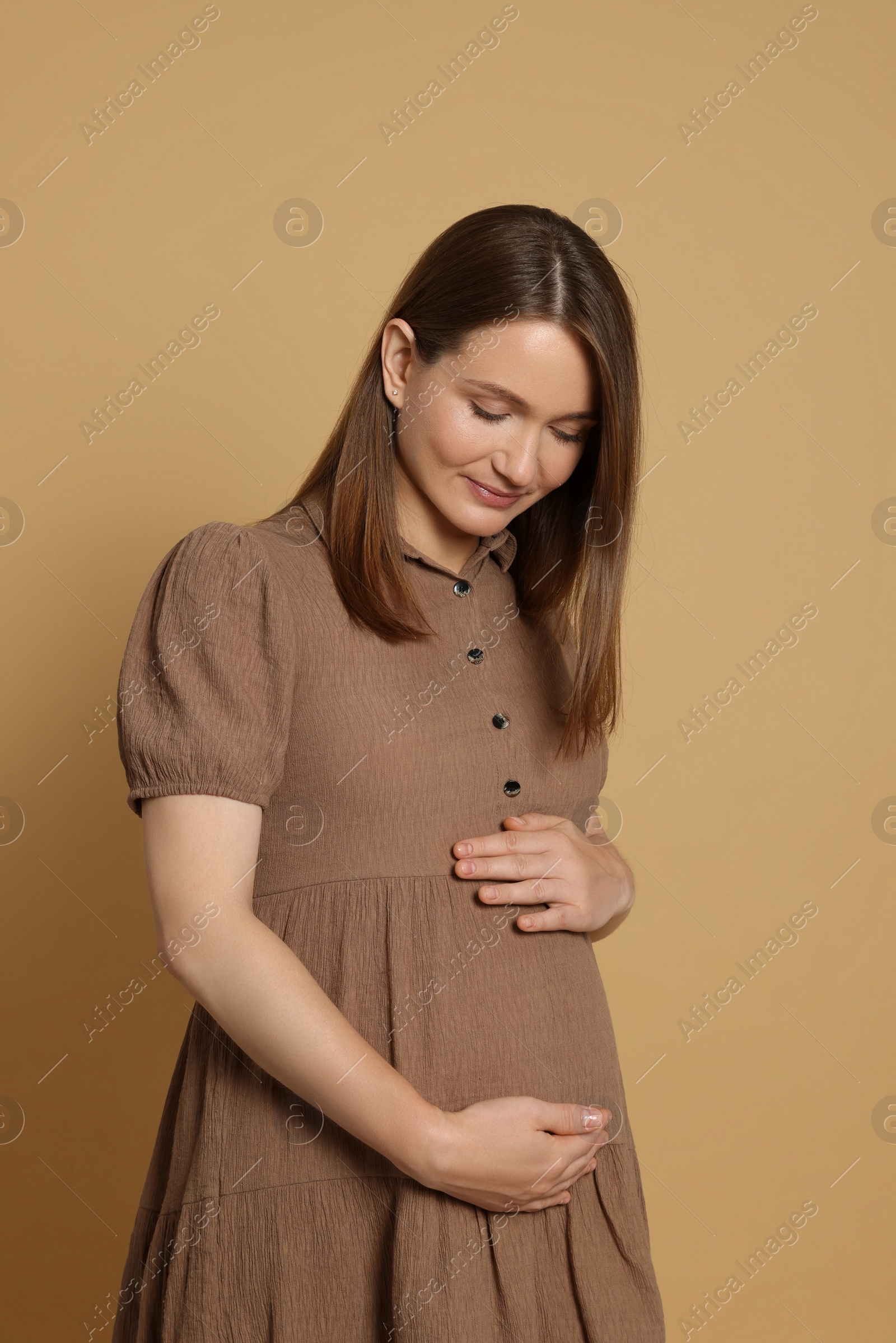 Photo of Happy young pregnant woman on light brown background