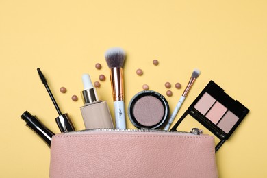 Cosmetic bag with makeup products and accessories on yellow background, flat lay