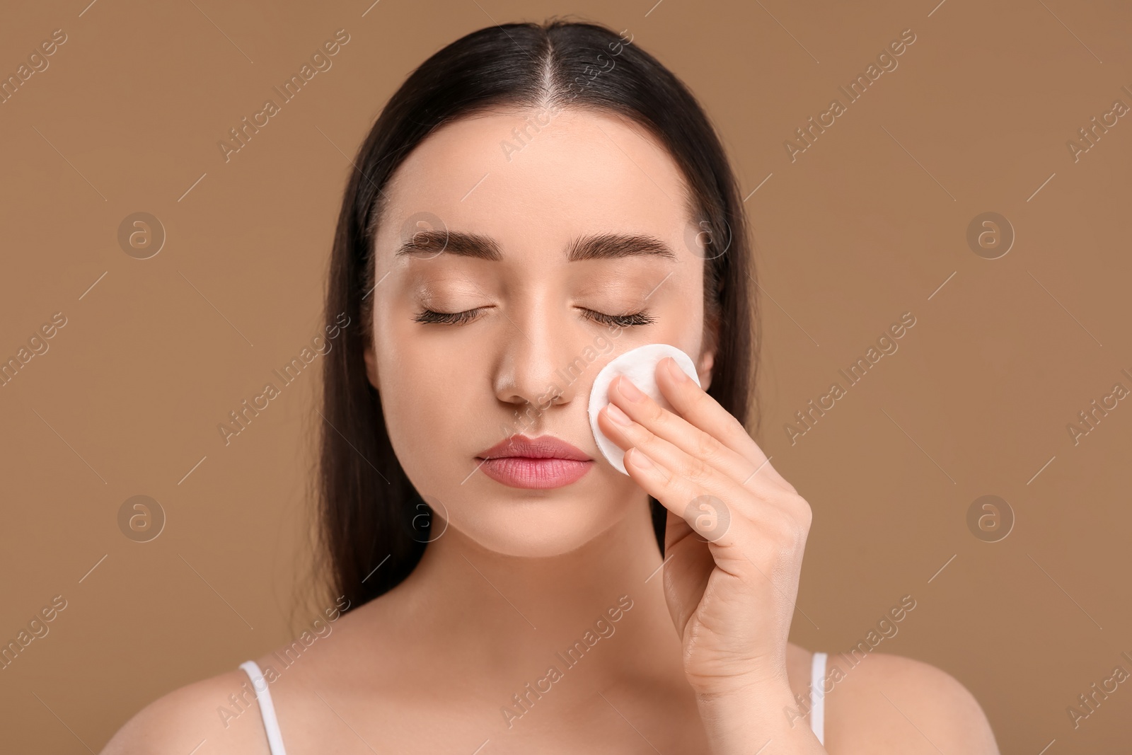 Photo of Beautiful woman removing makeup with cotton pad on beige background