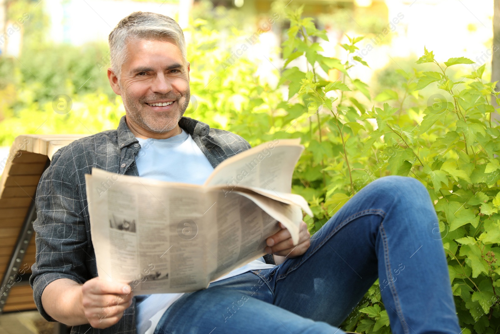 Photo of Handsome mature man with newspaper on bench in park