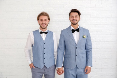 Happy newlywed gay couple in suits against white wall