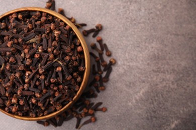 Aromatic cloves in bowl on brown table, top view. Space for text