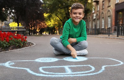 Photo of Child drawing car with chalk on asphalt