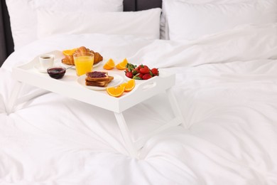 Photo of Tray with delicious breakfast on bed, closeup. Space for text
