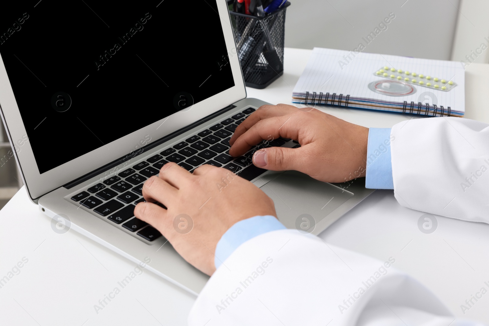 Photo of Doctor working with laptop at white desk in clinic, closeup. Online medicine