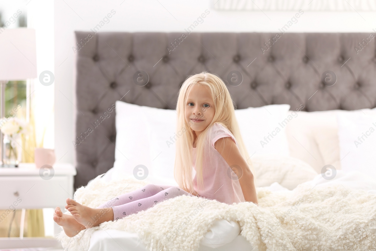 Photo of Cute little girl sitting on bed with pillows at home