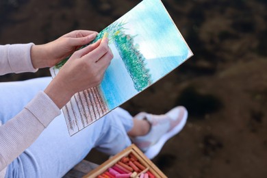 Photo of Woman drawing with soft pastels near river, closeup