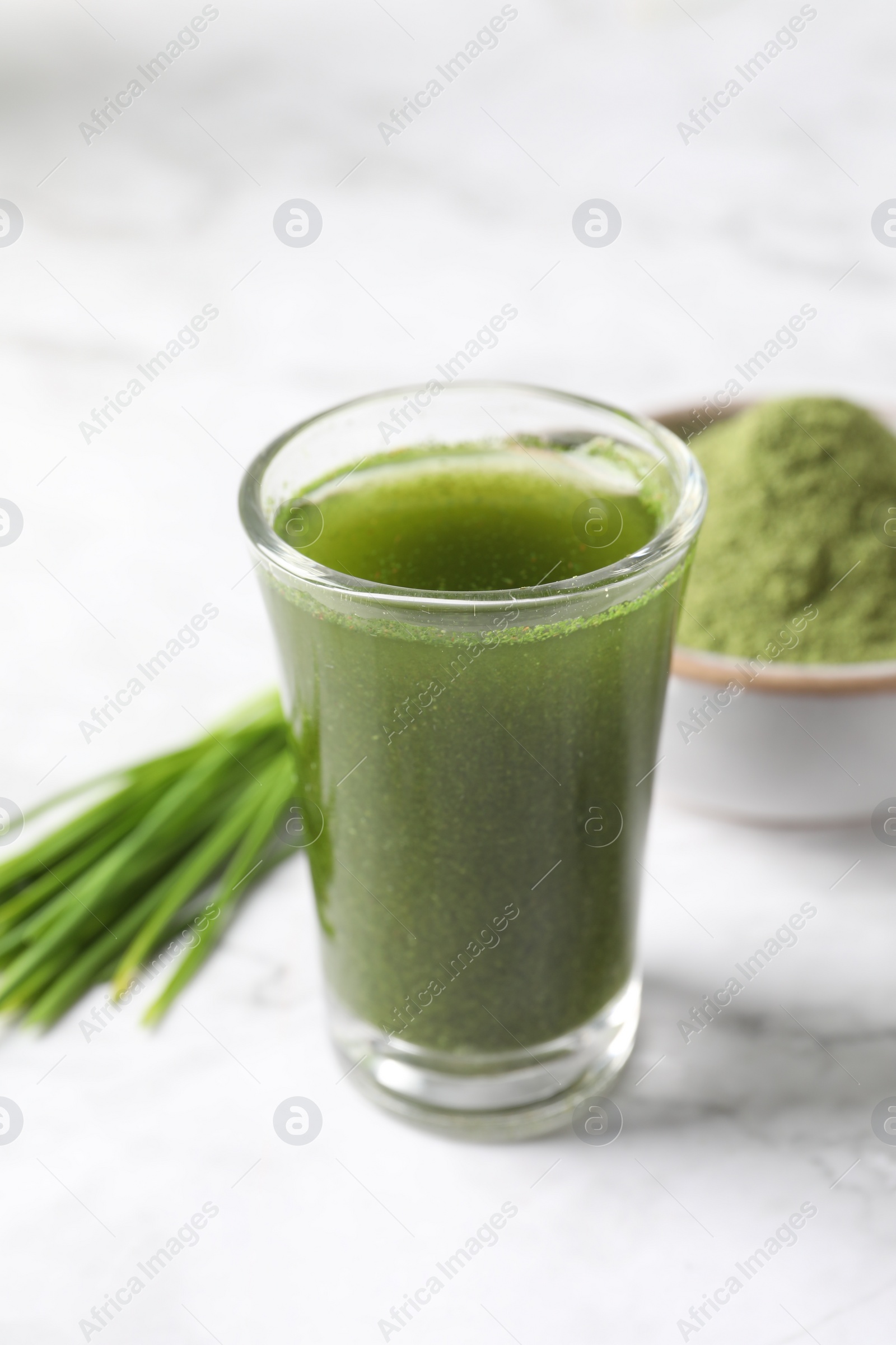 Photo of Wheat grass drink in shot glass on white marble table, closeup