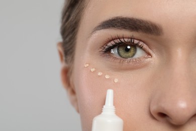 Photo of Young woman applying cream under eyes on white background, closeup