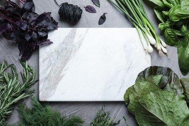 Photo of Different herbs and marble cutting board on grey table, flat lay. Space for text