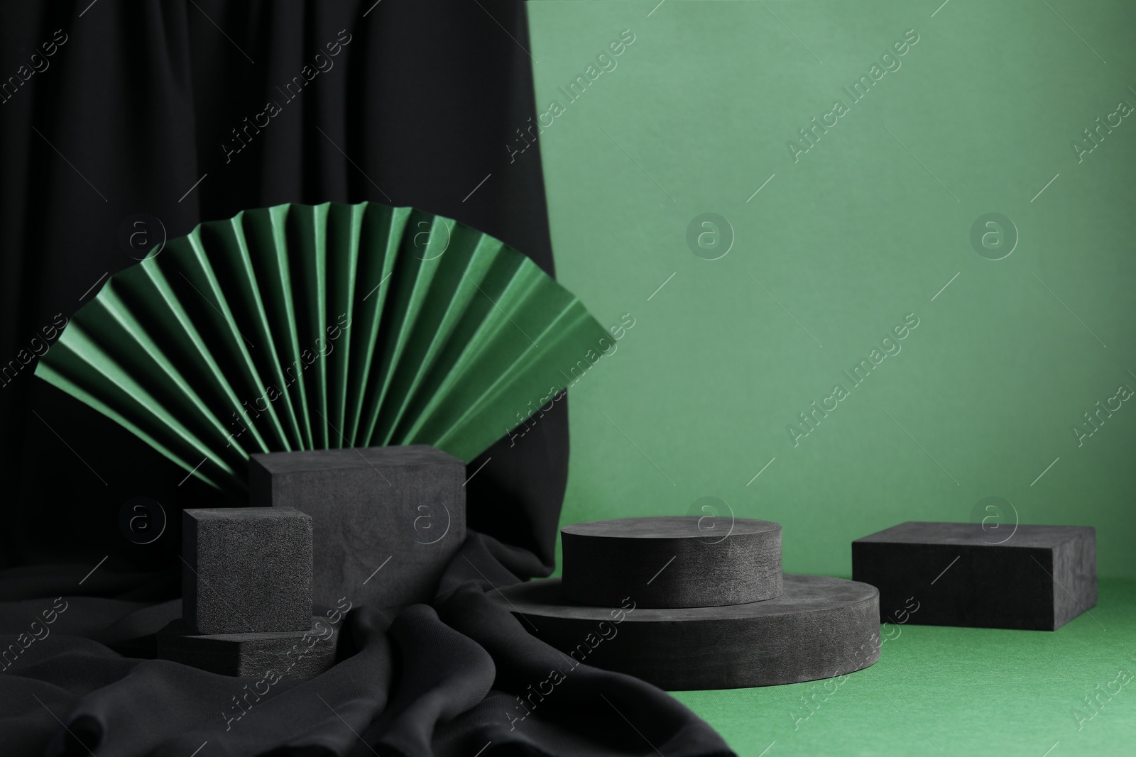 Photo of Black geometric figures and paper fan on green background. Stylish presentation for product