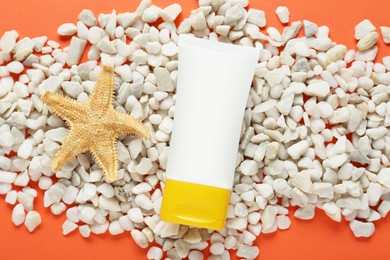 Tube of suntan cream, starfish and white marble pebbles on orange background, flat lay