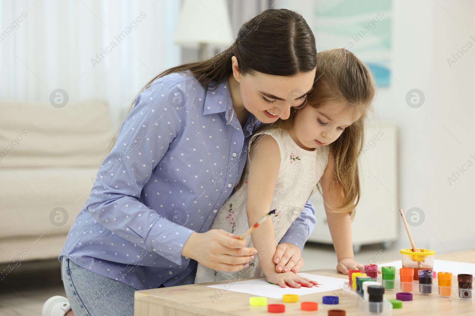 Photo of Mother and her little daughter painting with palms at home