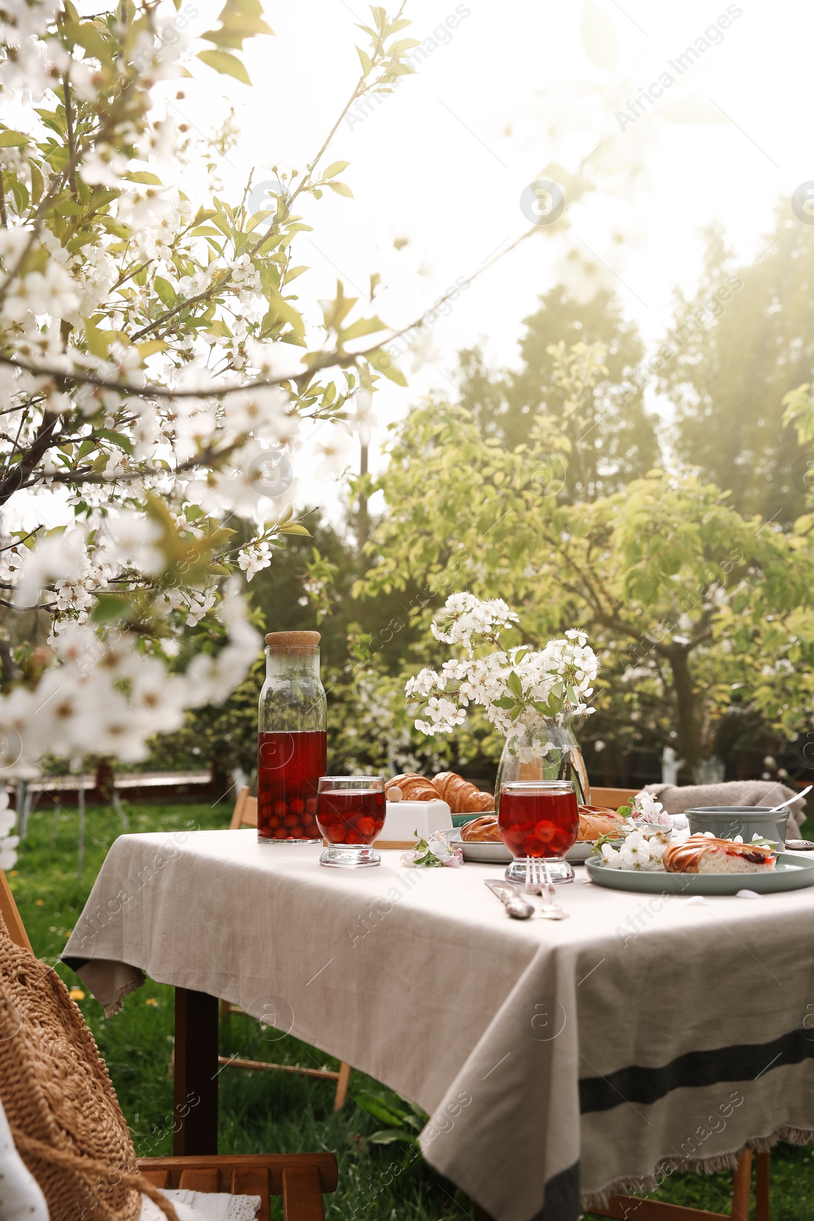 Photo of Stylish table setting with beautiful spring flowers, fruit drink and pie in garden