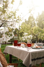 Stylish table setting with beautiful spring flowers, fruit drink and pie in garden