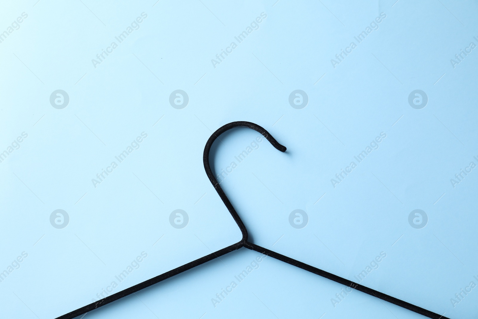 Photo of One black hanger on light blue background, top view. Space for text