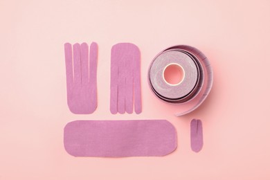 Photo of Bright kinesio tape roll and pieces on pink background, flat lay