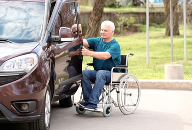 Mature man in wheelchair opening door of his van outdoors