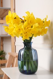 Beautiful daffodils in vase on white table indoors. Fresh spring flowers