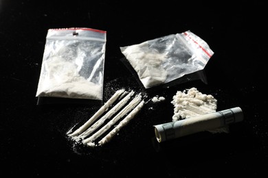 Photo of Drug addiction. Plastic bags with cocaine and rolled dollar banknote on black table, closeup