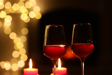 Photo of Glasses of wine and candles against blurred lights, closeup with space for text. Romantic dinner
