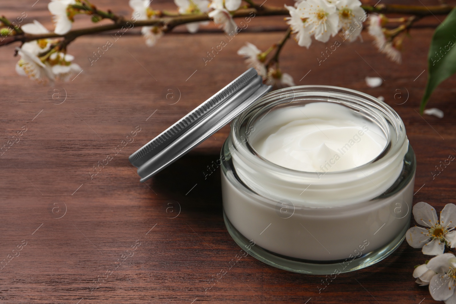 Photo of Jar of face cream and flowers on wooden table. Space for text