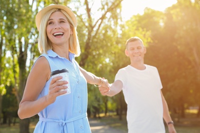 Photo of Happy couple with drink walking along park on summer day