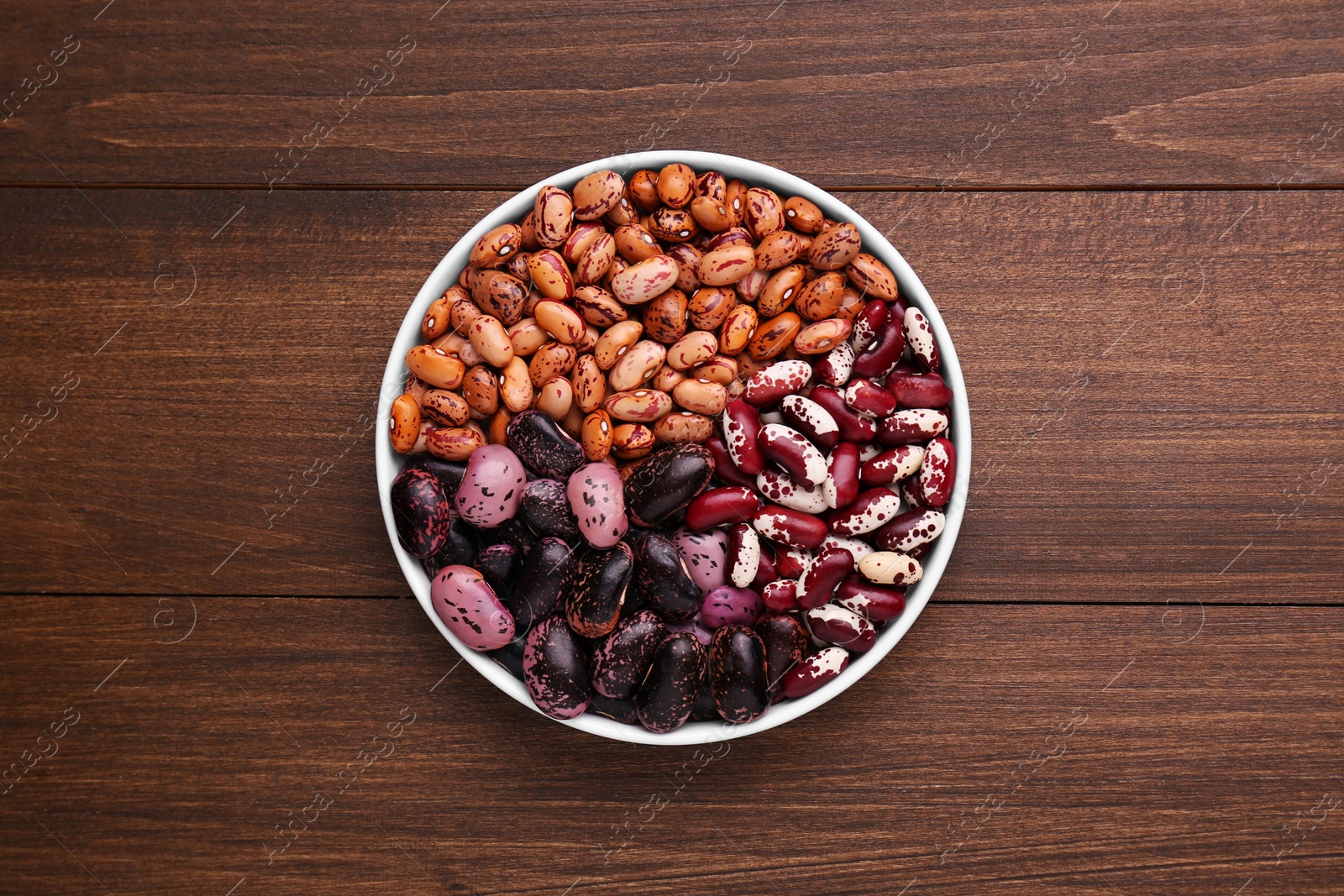 Photo of Different kinds of dry kidney beans in bowl on wooden table, top view