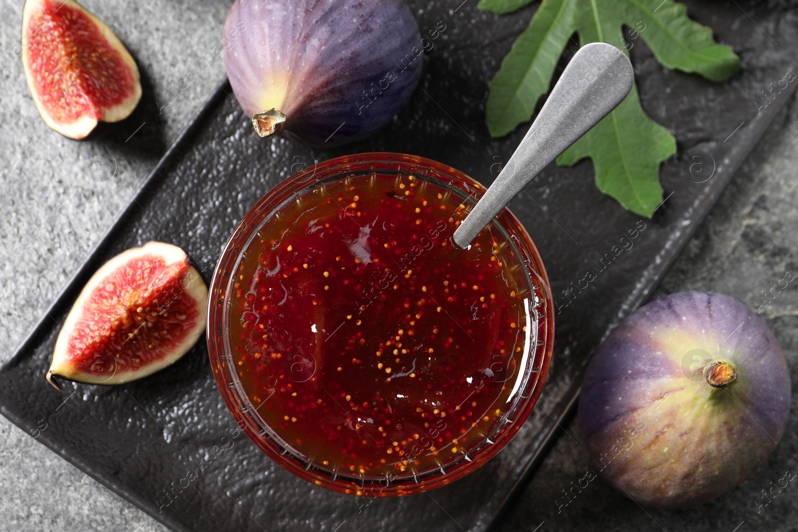 Photo of Glass bowl with tasty sweet jam and fresh figs on grey table, flat lay