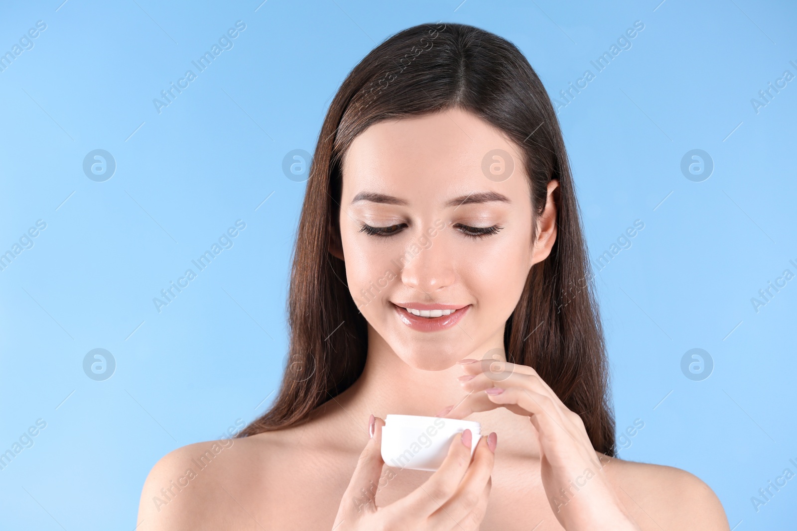 Photo of Teenage girl with acne problem using cream against color background