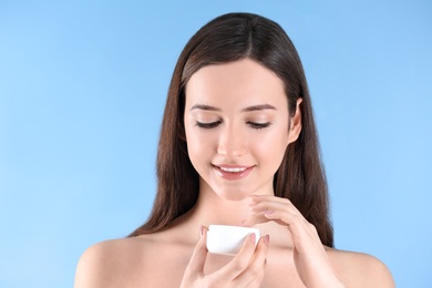 Teenage girl with acne problem using cream against color background