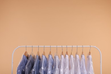 Photo of Dry-cleaning service. Many different clothes in plastic bags hanging on rack against beige background, space for text